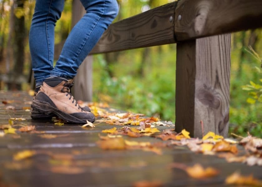 A person stands on a wooden path covered with autumn leaves, wearing hiking boots and jeans. A person stands on a wooden path covered with autumn leaves, wearing hiking boots and jeans.