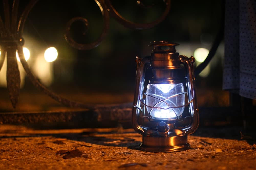 A lit antique lantern glowing softly on a gravel surface at night.