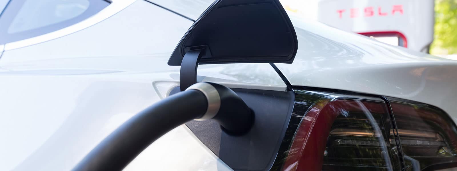 A white Tesla car charging at a charging station.