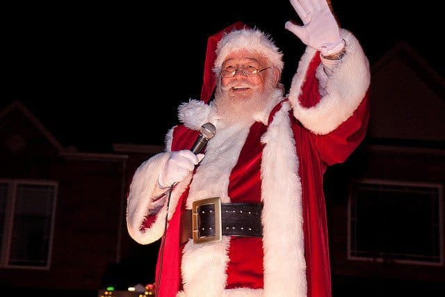 A cheerful Santa Claus waves while holding a microphone. A cheerful Santa Claus waves while holding a microphone.