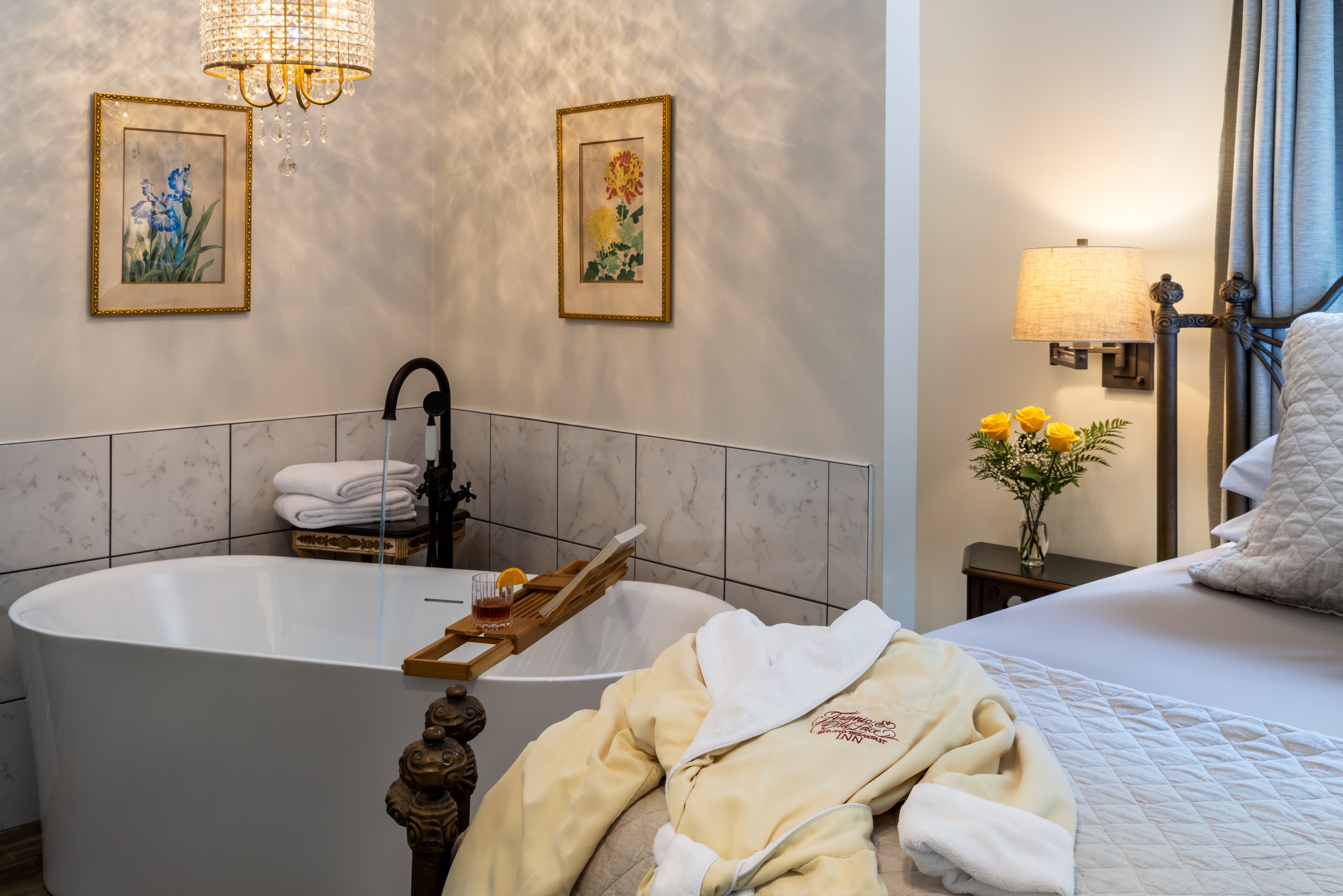 A cozy bathroom featuring a freestanding tub, bathrobe, artwork, and a bouquet of yellow flowers.