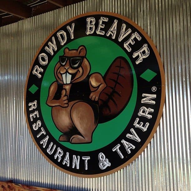 A circular sign featuring a cartoon beaver wearing sunglasses, promoting the Rowdy Beaver Restaurant & Tavern. A circular sign featuring a cartoon beaver wearing sunglasses, promoting the Rowdy Beaver Restaurant & Tavern.