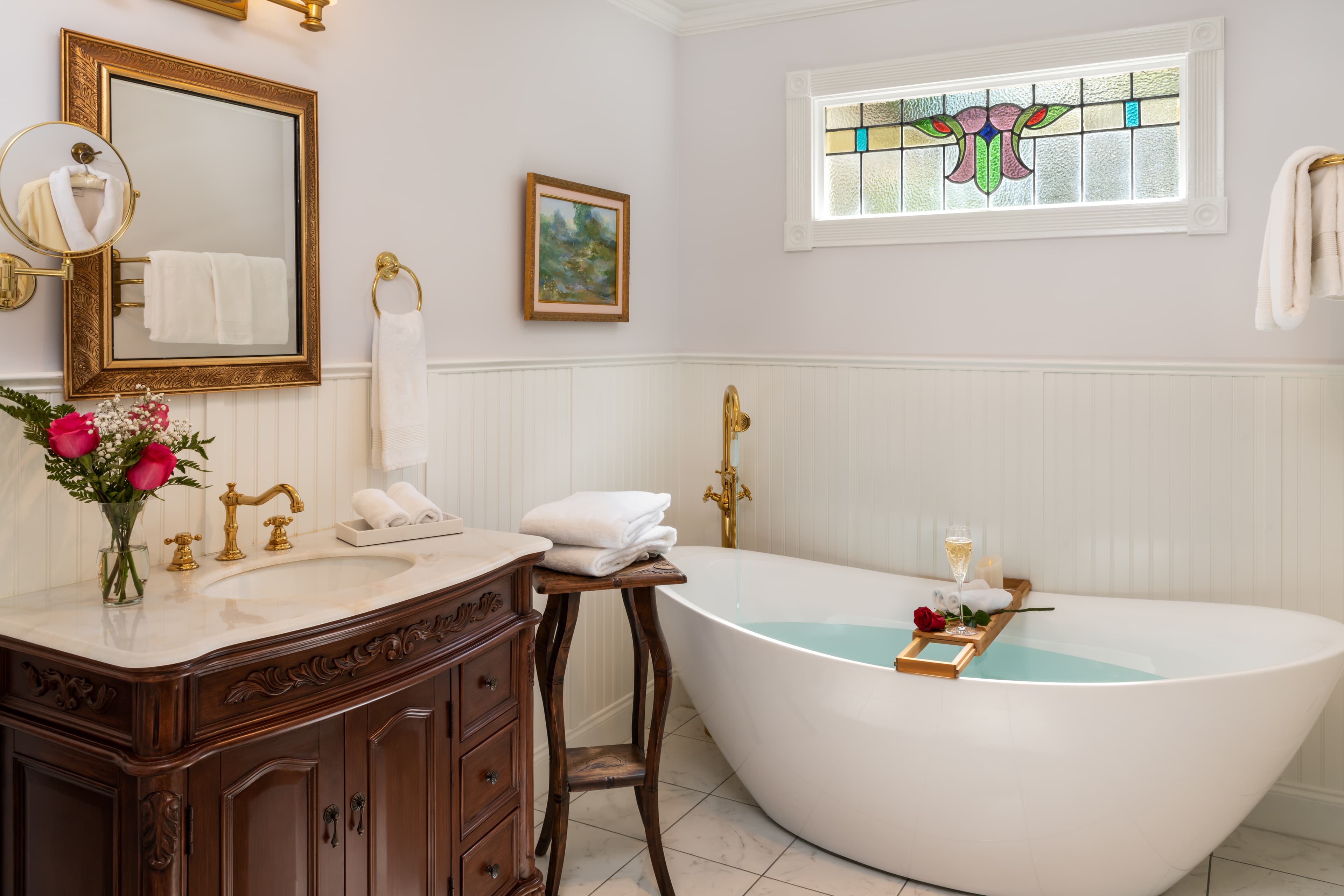 A stylish bathroom featuring a freestanding tub, elegant fixtures, and a charming stained glass window.
