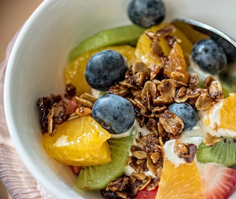 A bowl of yogurt topped with granola, blueberries, kiwi slices, and orange segments.