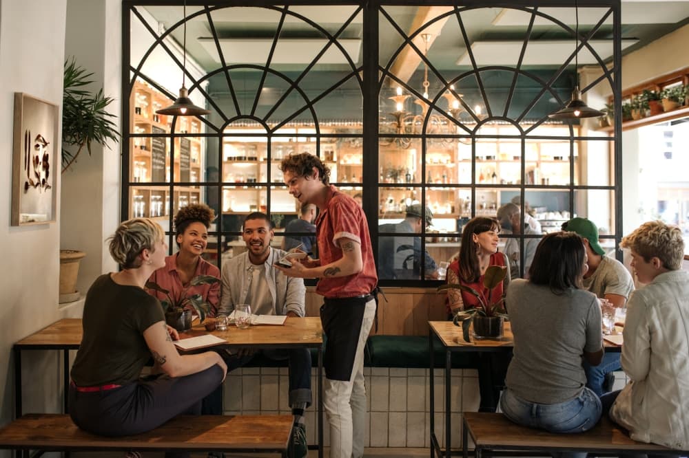 A group of diners enjoys a meal at a lively restaurant, with a waiter serving them. A group of diners enjoys a meal at a lively restaurant, with a waiter serving them.