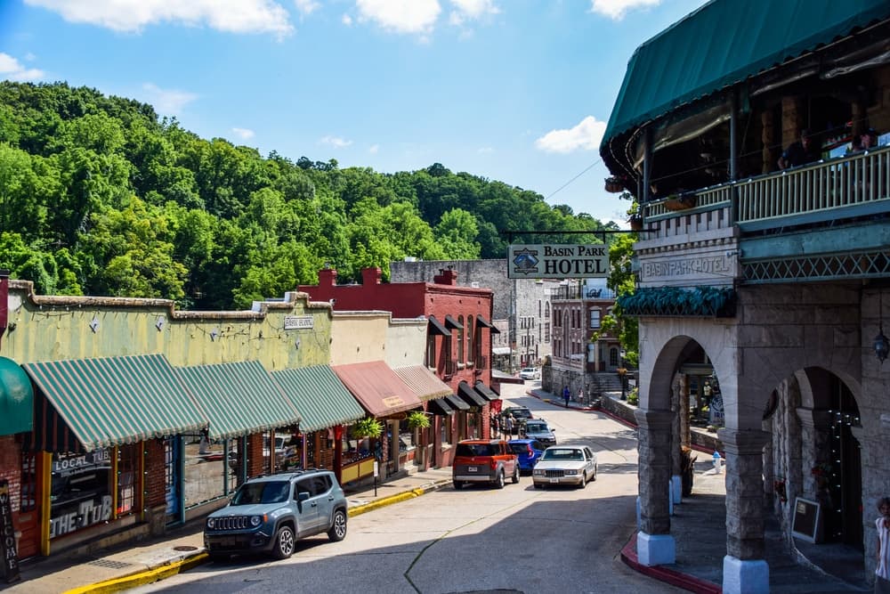 A picturesque street lined with boutiques and a hotel, framed by lush greenery on a sunny day.