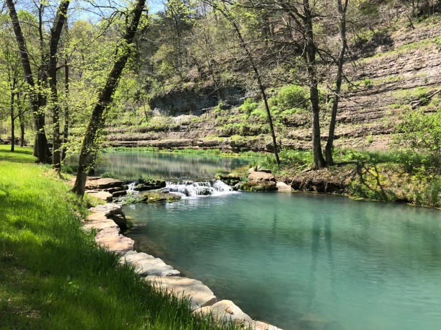 A serene river flows through a lush green landscape, surrounded by trees and gentle rock formations.