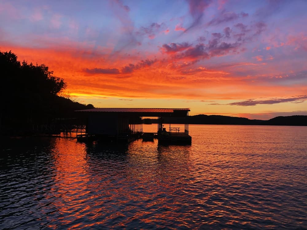 A silhouette of a dock against a vibrant sunset with orange, pink, and purple hues reflected in the water.