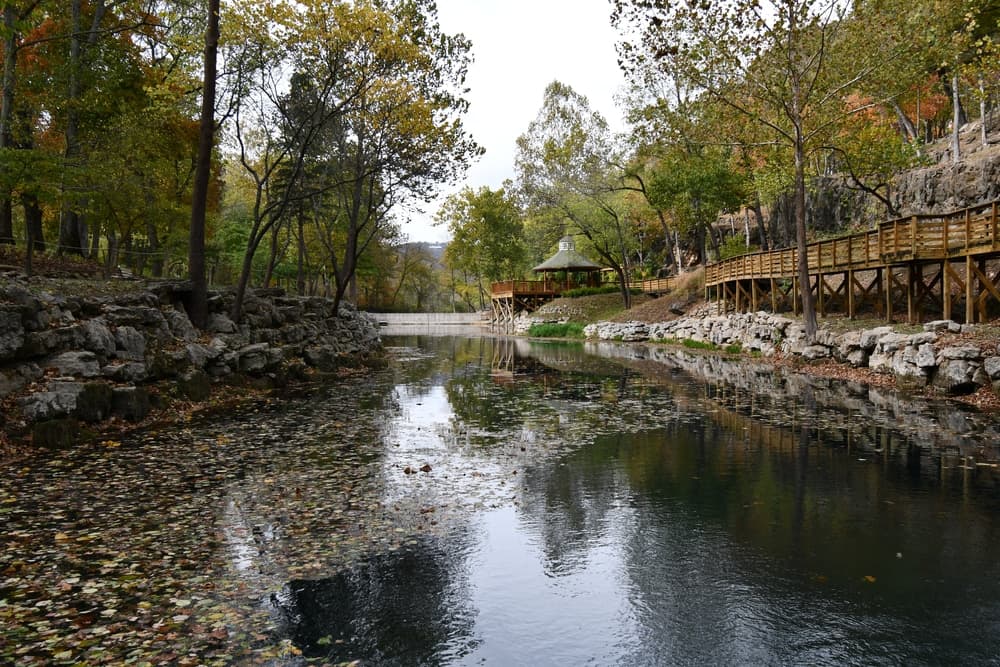 A tranquil river surrounded by autumn trees and a wooden walkway.