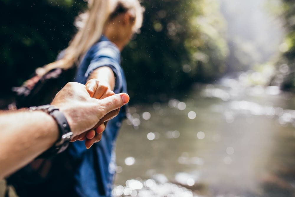 A person reaches out to hold another's hand by a river, with a blurred background.