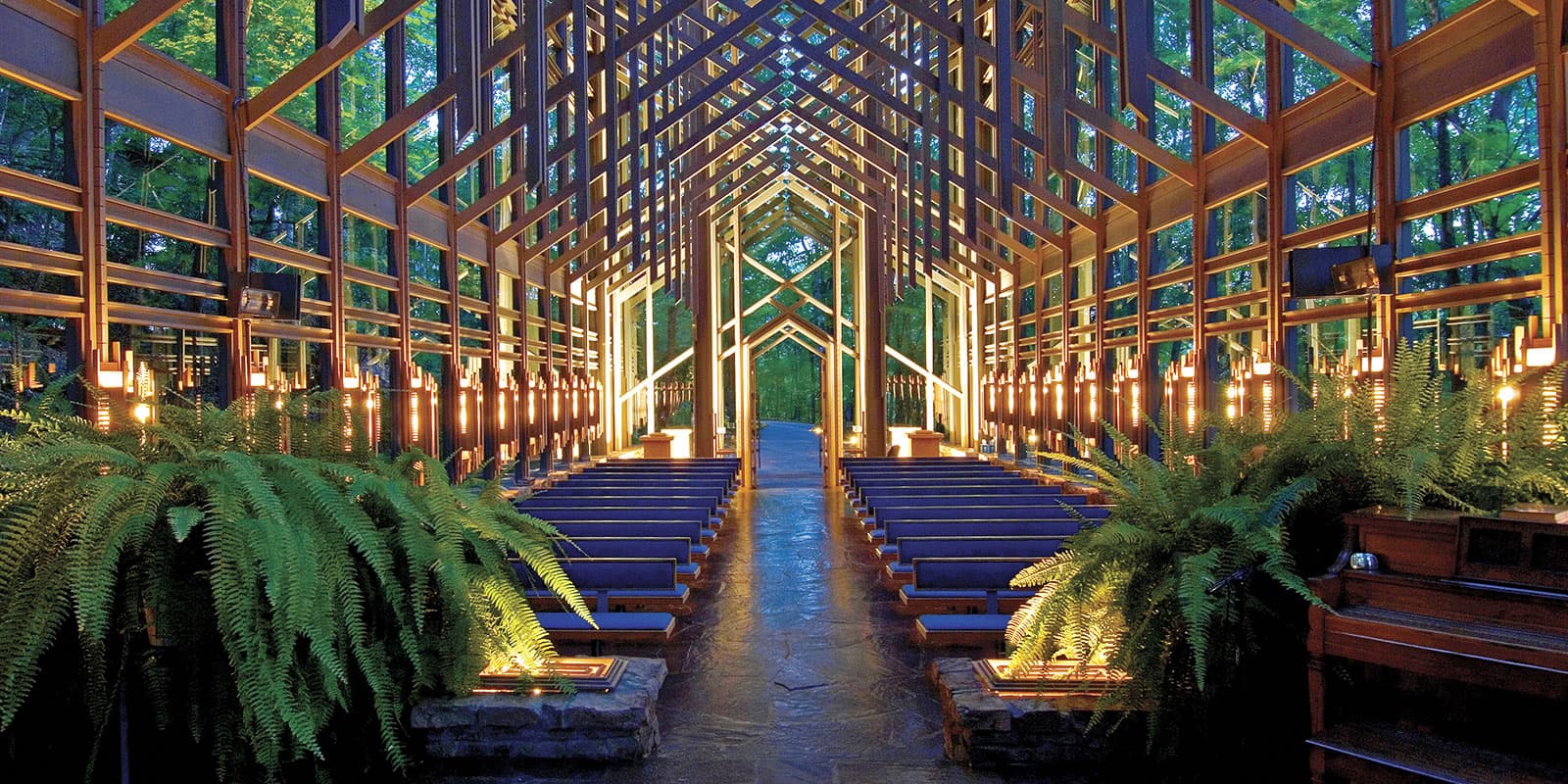 A beautifully designed glass and wood chapel surrounded by greenery.