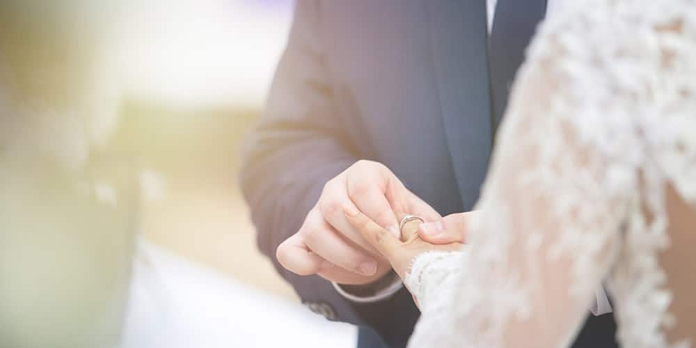 A person placing a wedding ring on their partner's finger during a ceremony.