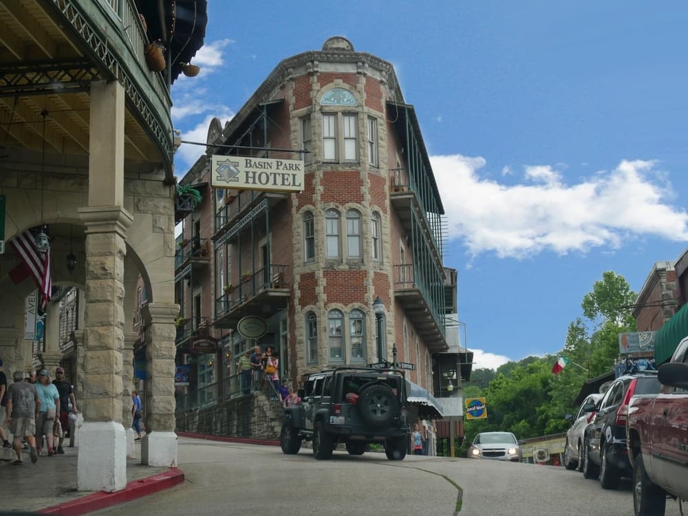 A scenic view of Basin Park Hotel with pedestrians and cars on a sloping street under a blue sky.