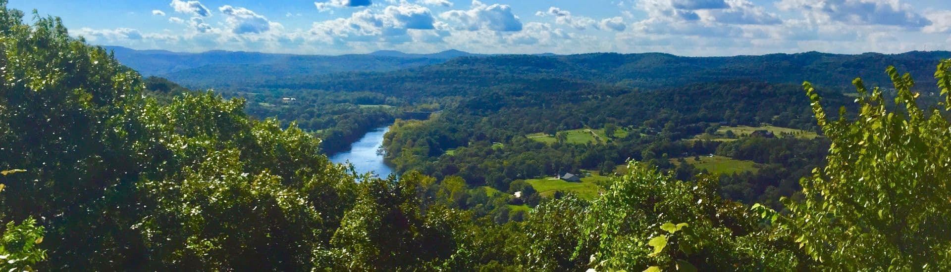 Vast valley lush with green trees, rolling hills, river and blue skies with clouds above