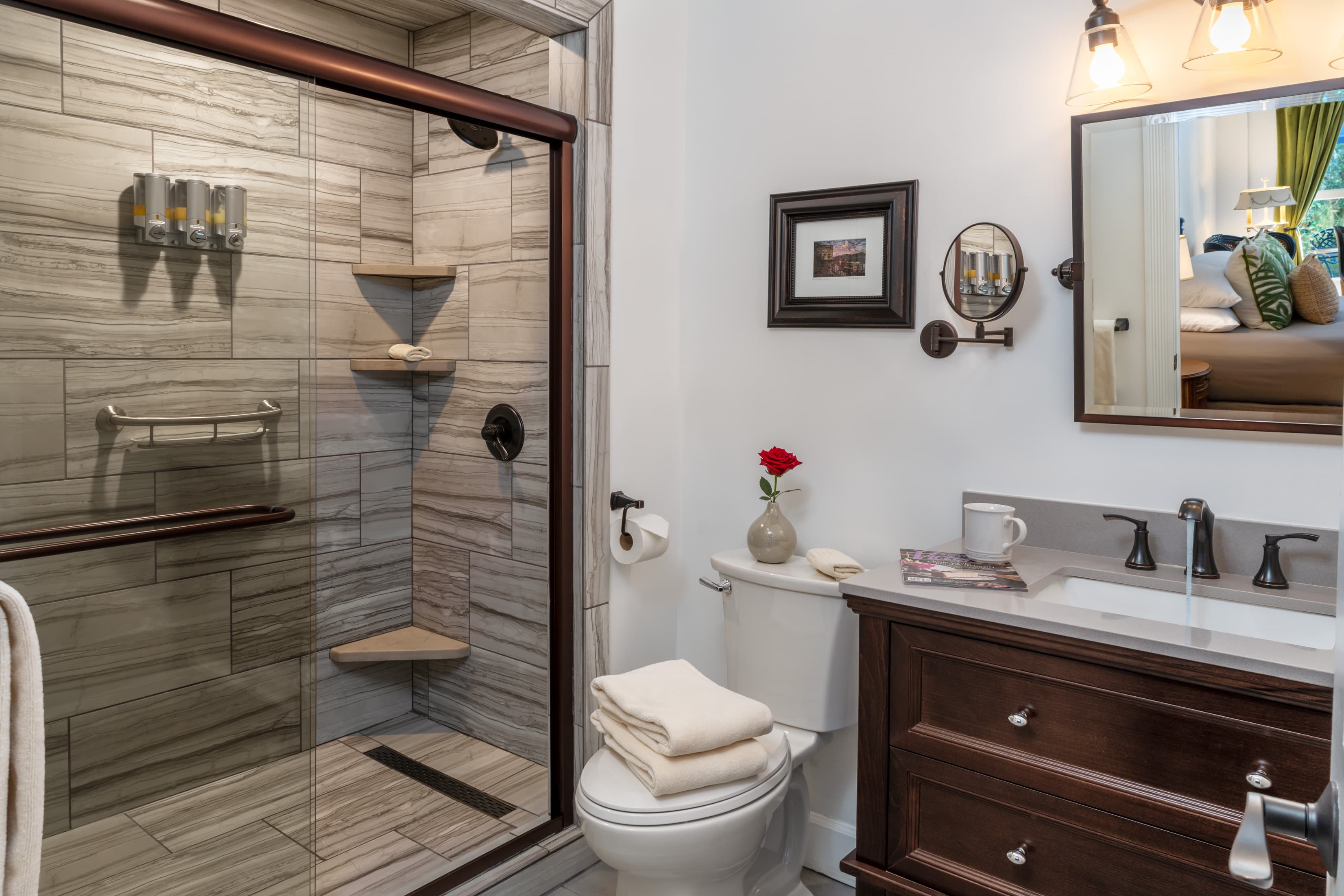 A modern bathroom featuring a glass shower, dark wood vanity, and decorative accents.