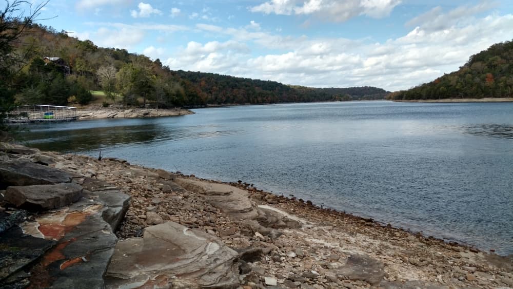 A tranquil lake surrounded by rolling hills and a rocky shoreline under a partly cloudy sky.