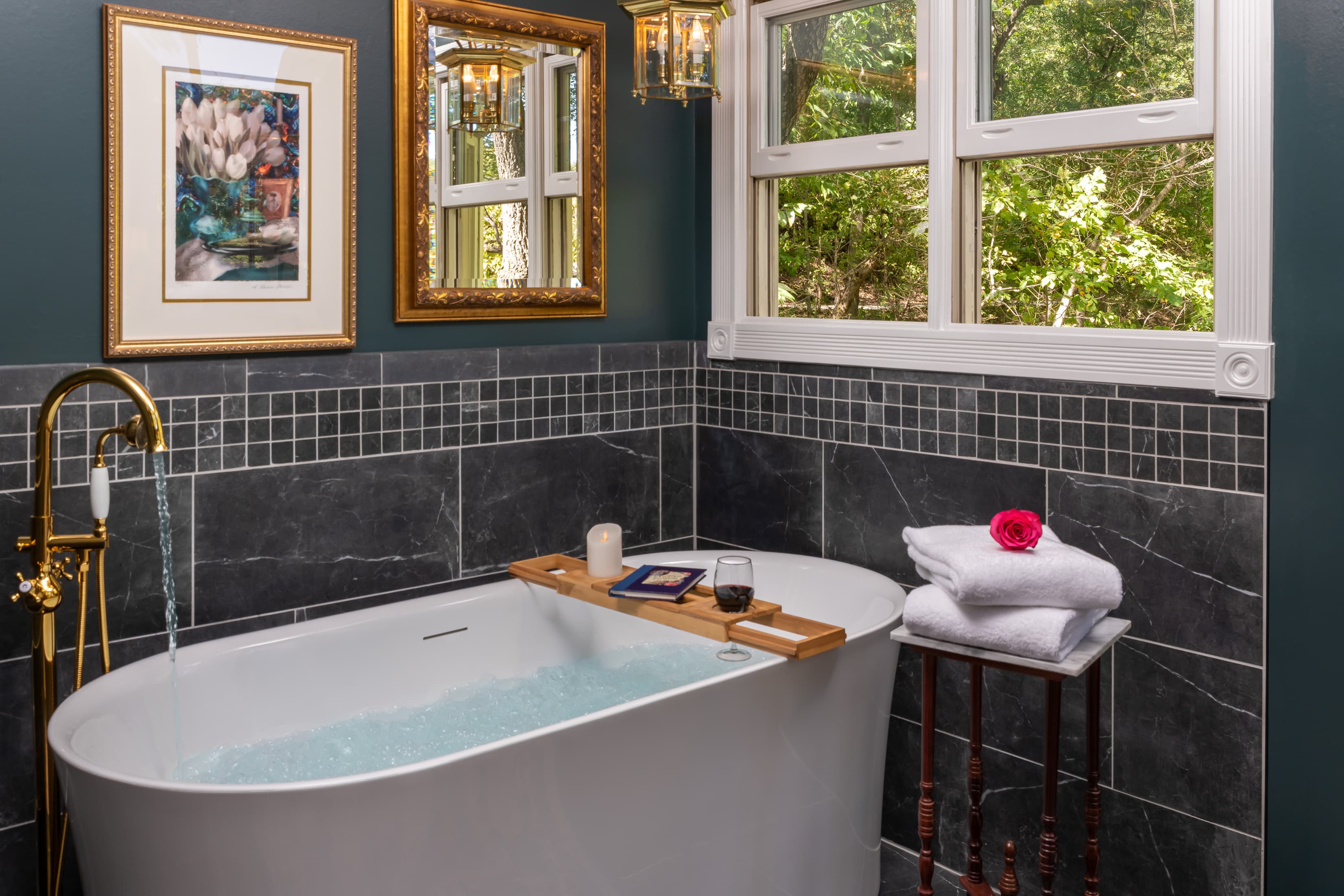 A luxurious bathroom featuring a freestanding tub, soothing blue water, and natural light from windows.