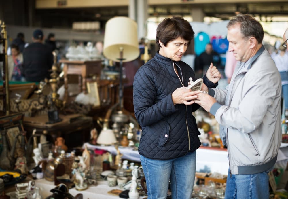 A woman and man examine a small decorative item amidst various antiques at a market.