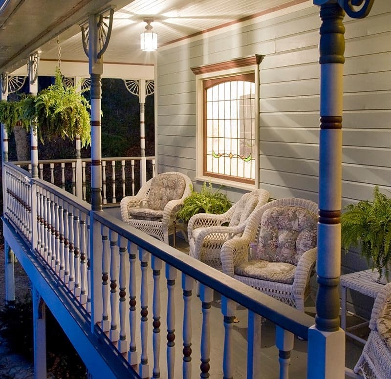 A cozy porch with wicker chairs and ferns, illuminated by a hanging light.