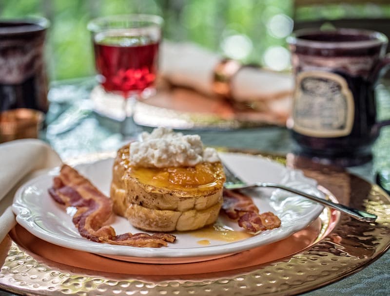 A plate featuring a thick slice of French toast topped with ricotta cheese and fruit.