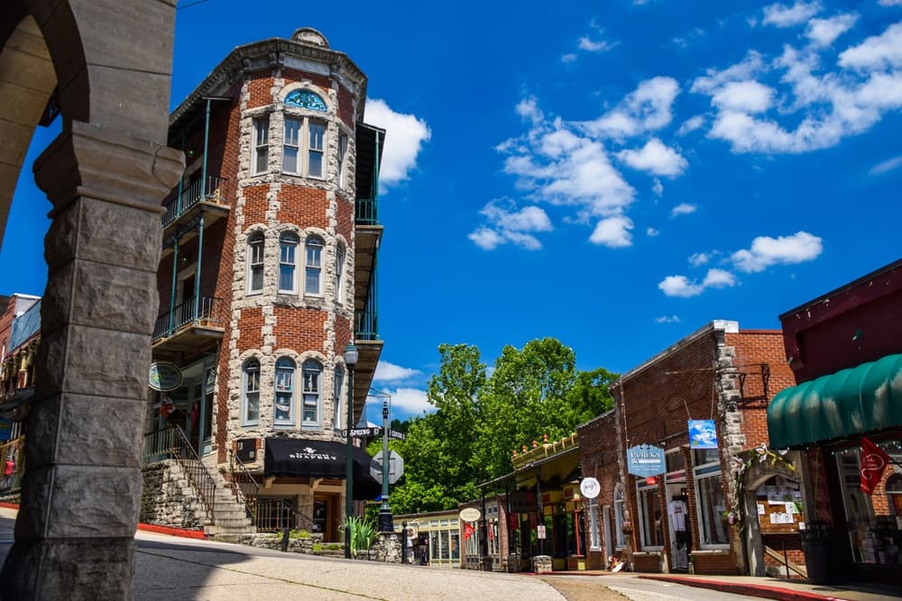Historic brick building with a rounded tower, surrounded by shops under a bright blue sky.