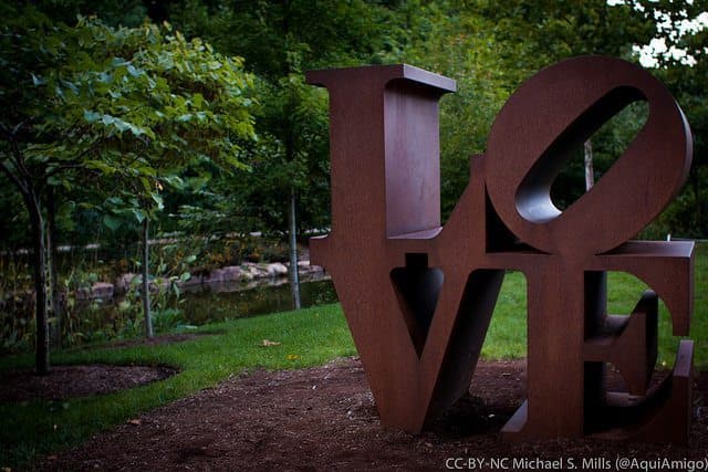 A large, rust-colored sculpture of the word "LOVE" surrounded by greenery.