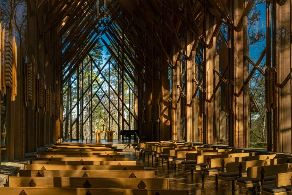 A modern wooden chapel interior with rows of benches and large glass windows allowing natural light to flood in.