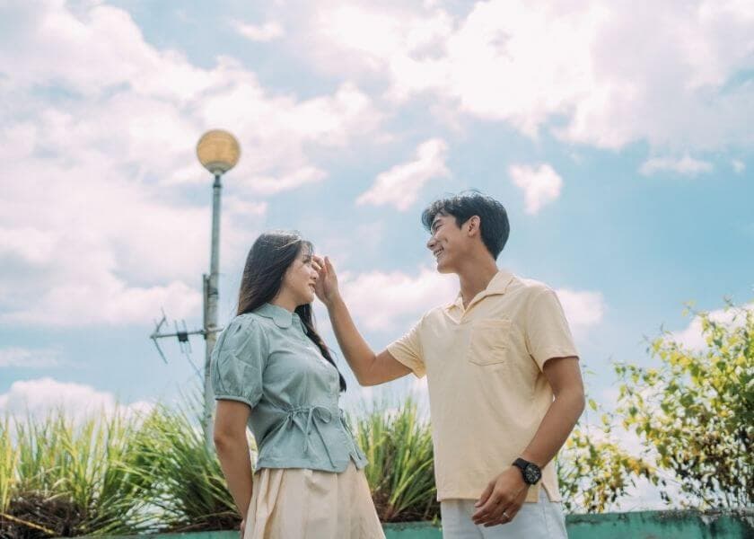 A young couple smiles at each other against a bright sky and greenery. A young couple smiles at each other against a bright sky and greenery.