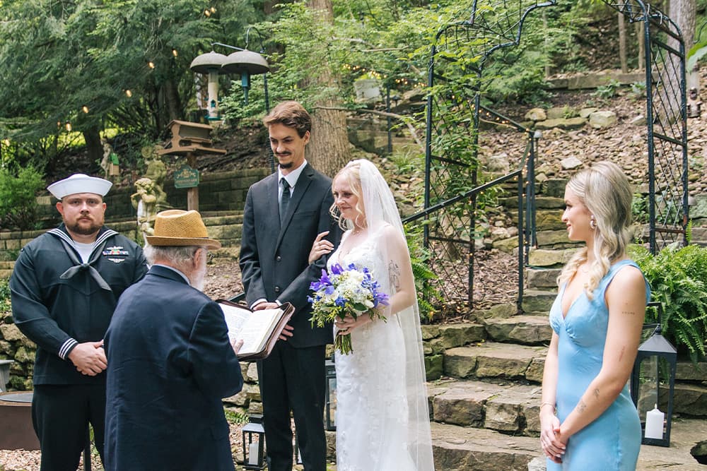 Couple getting married in beautiful natural surroundings with little twinkle lights hanging from the trees behind them.