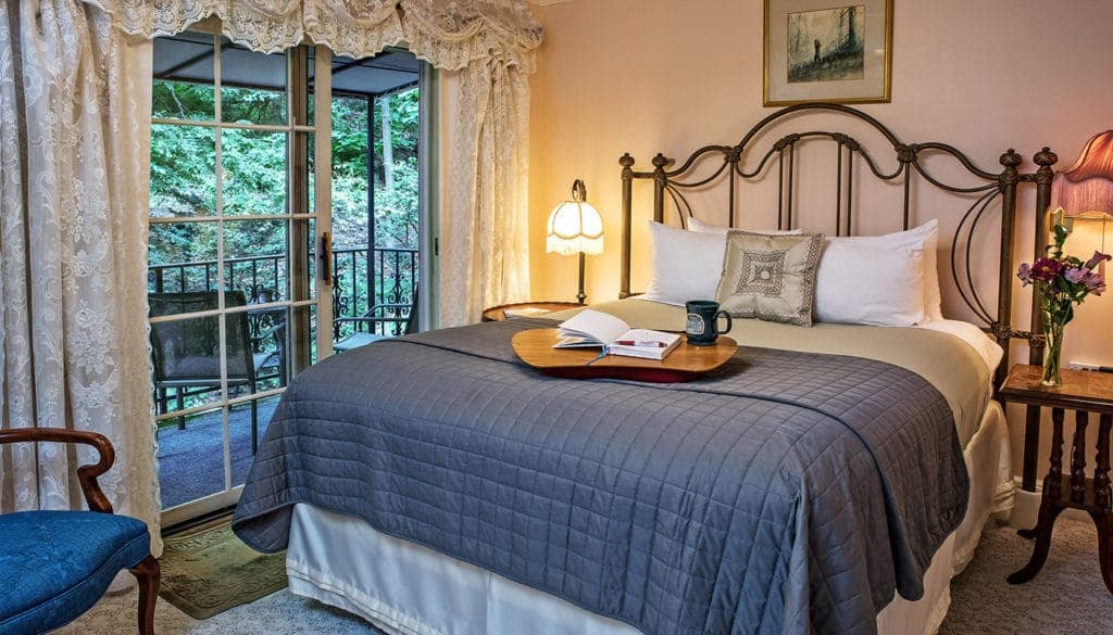 Cozy bedroom with a neatly made bed, a side table with a book and mug, and a balcony visible through glass doors.