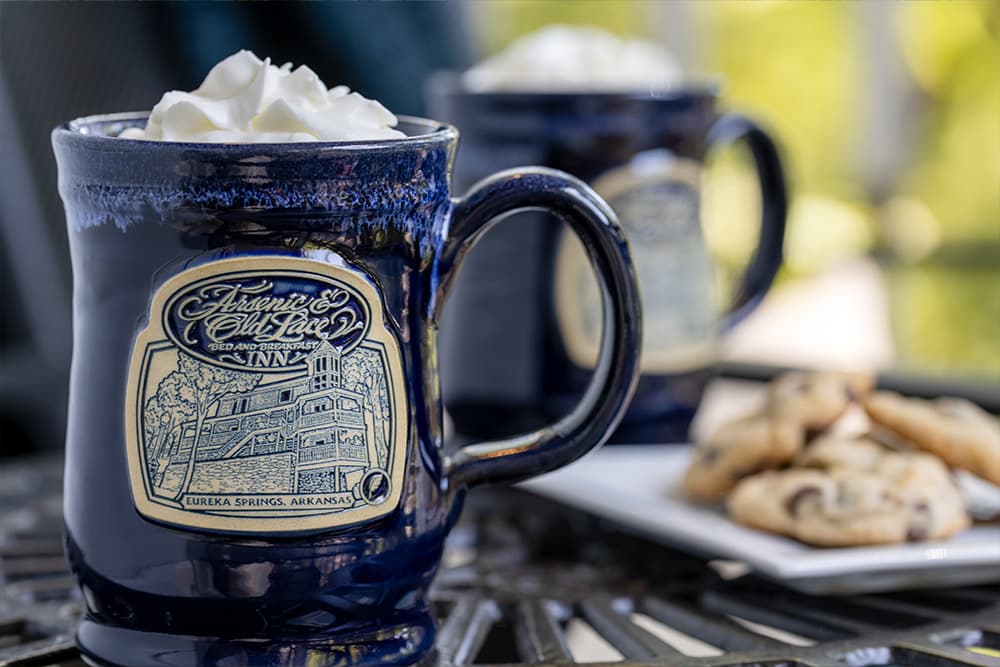 Two mugs of hot chocolate with whipped cream and cookies on a plate.