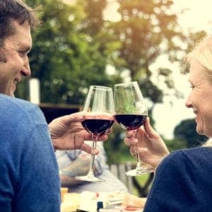 Two people clink wine glasses together outdoors, celebrating joyfully.