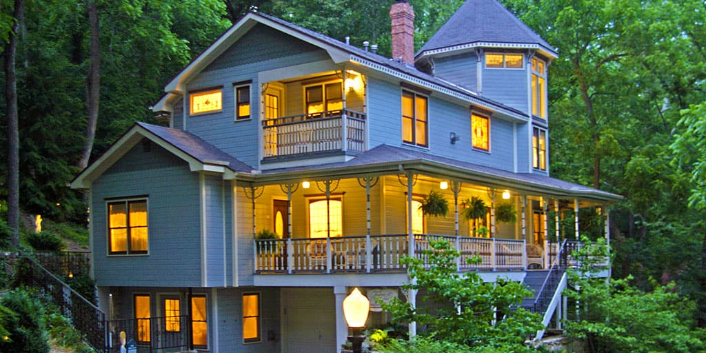 A charming blue house with large windows and a wraparound porch, surrounded by lush green trees. A charming blue house with large windows and a wraparound porch, surrounded by lush green trees.