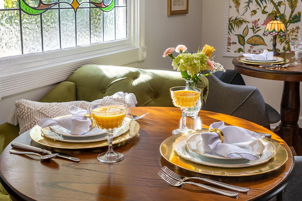 A cozy dining area with a round table set for two. The table is decorated with a floral arrangement and features elegant place settings.