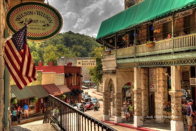 Quaint shops line a charming street under a cloudy sky, with a hotel sign visible in the background.