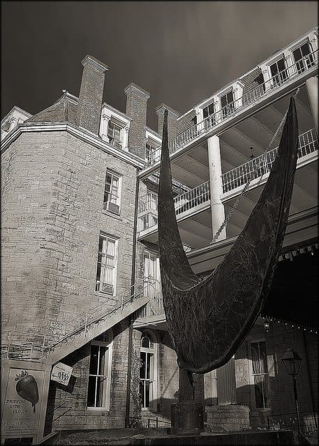 A large, abstract sculpture stands in front of a historic stone building with balconies.