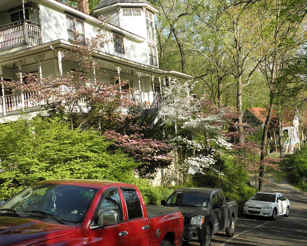 A tree-lined street featuring a white house with blooming dogwood trees and parked cars. A tree-lined street featuring a white house with blooming dogwood trees and parked cars.