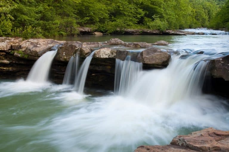 A serene waterfall cascading over rocky ledges into a calm river, surrounded by lush greenery. A serene waterfall cascading over rocky ledges into a calm river, surrounded by lush greenery.