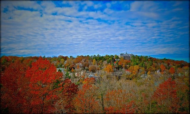 Vibrant autumn foliage covers a hillside under a blue sky with scattered clouds.