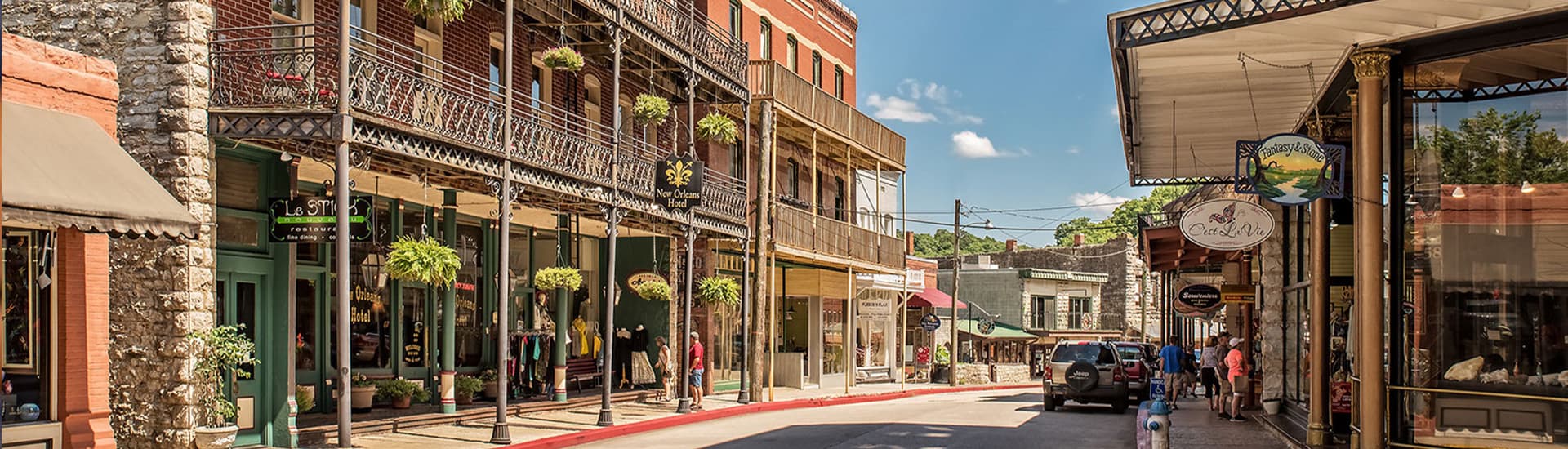 A narrow street in Eureka Springs, Arkansas, with colorful storefronts and hanging plants.