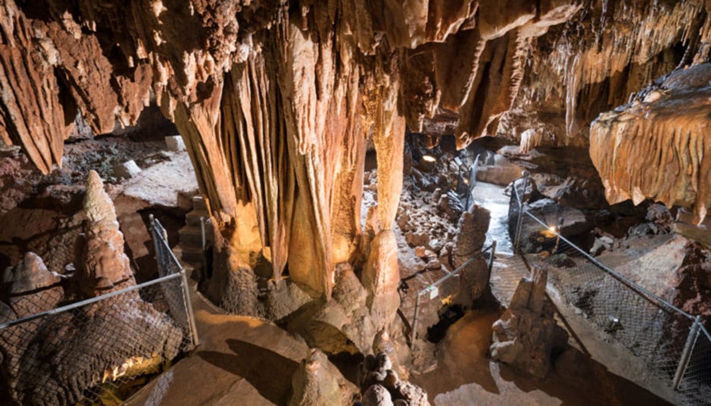 An illuminated cave interior featuring stalactites and stalagmites.