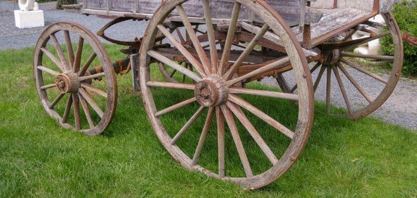 An old wooden wagon with large, weathered wheels sits on grass.