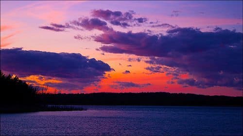A vibrant sunset with purple and orange hues reflecting over a calm lake.