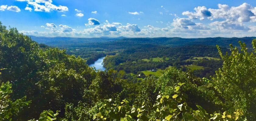 A scenic view of a river winding through lush green hills under a partly cloudy sky.