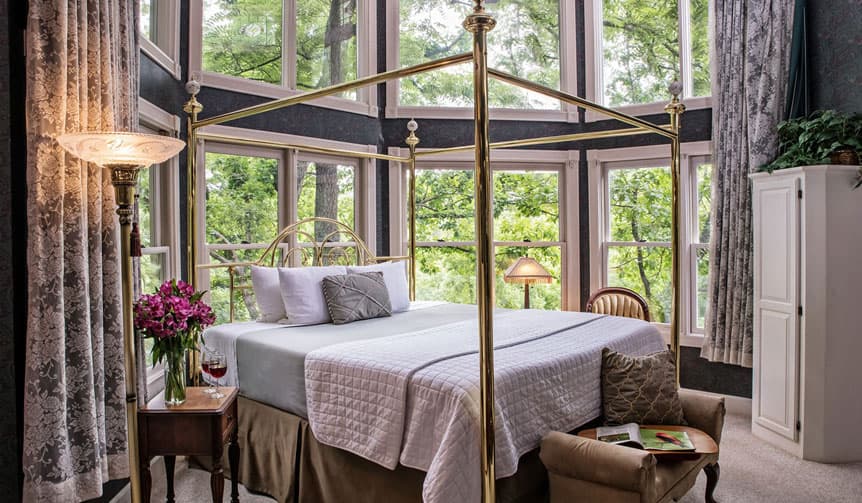 Cozy bedroom with a four-poster bed and large windows surrounded by greenery.