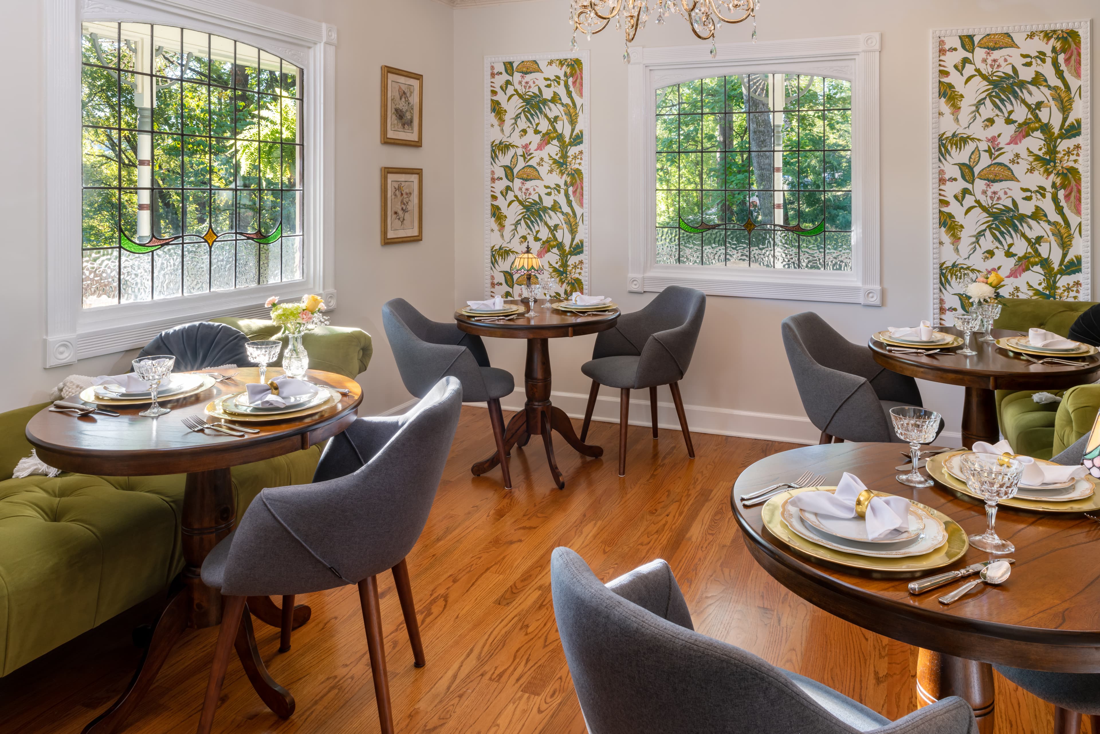 A cozy dining room with large windows, stained glass, and floral wallpaper.
