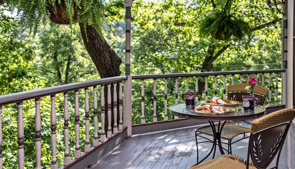 A cozy dining table set on a lush green balcony surrounded by trees.