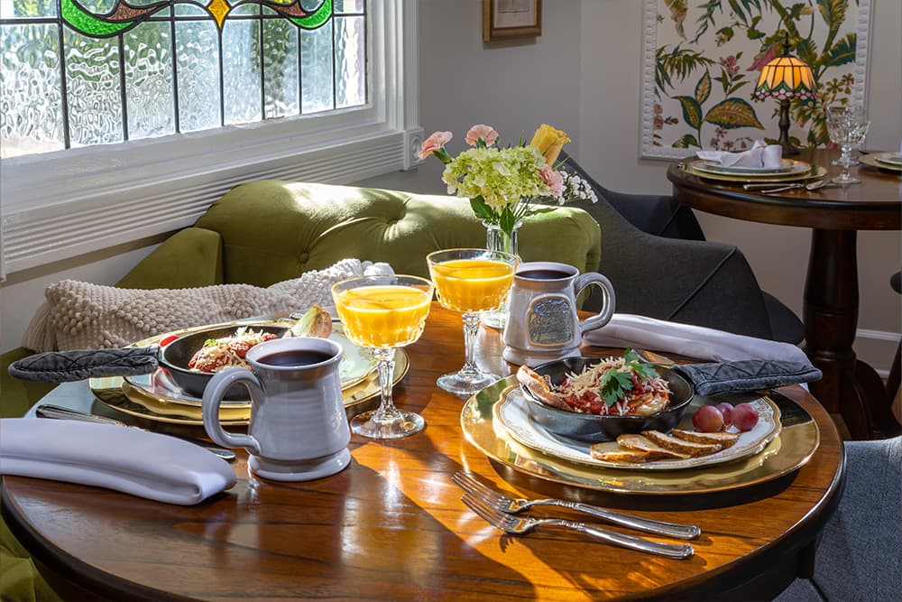 A cozy dining table set with breakfast dishes, including a skillet meal, toast, fruit, and glasses of juice.