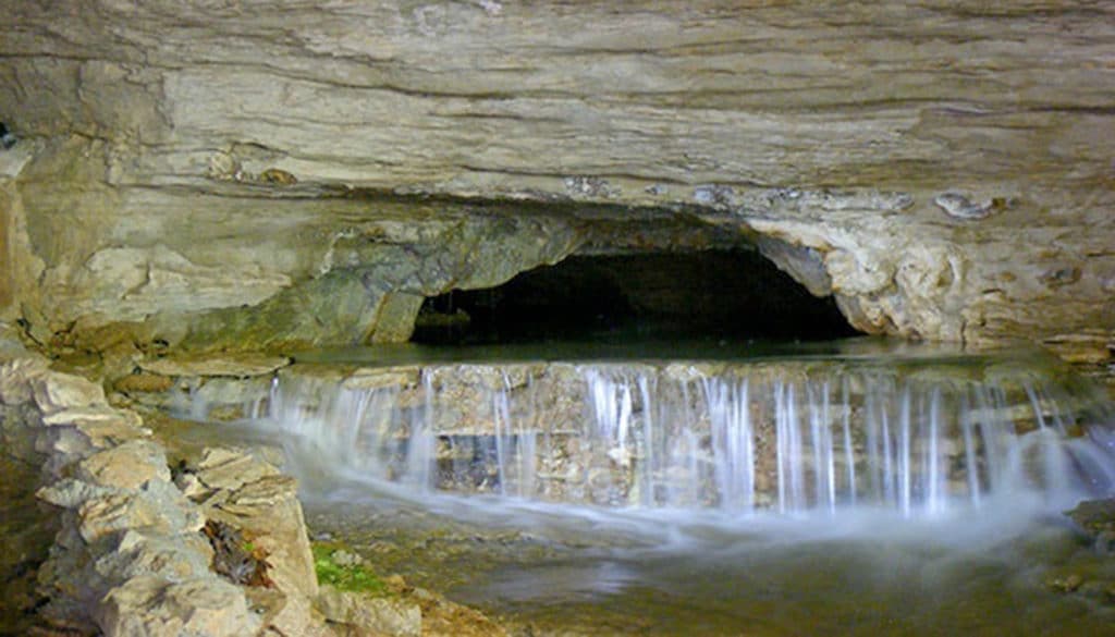 A small waterfall flows through a rocky cave opening.