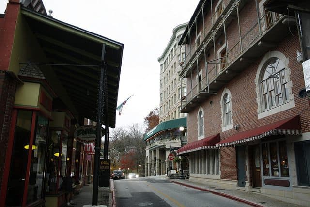 A quiet street scene featuring a mix of brick buildings, shops, and a hotel with awnings, set against an overcast sky. A quiet street scene featuring a mix of brick buildings, shops, and a hotel with awnings, set against an overcast sky.